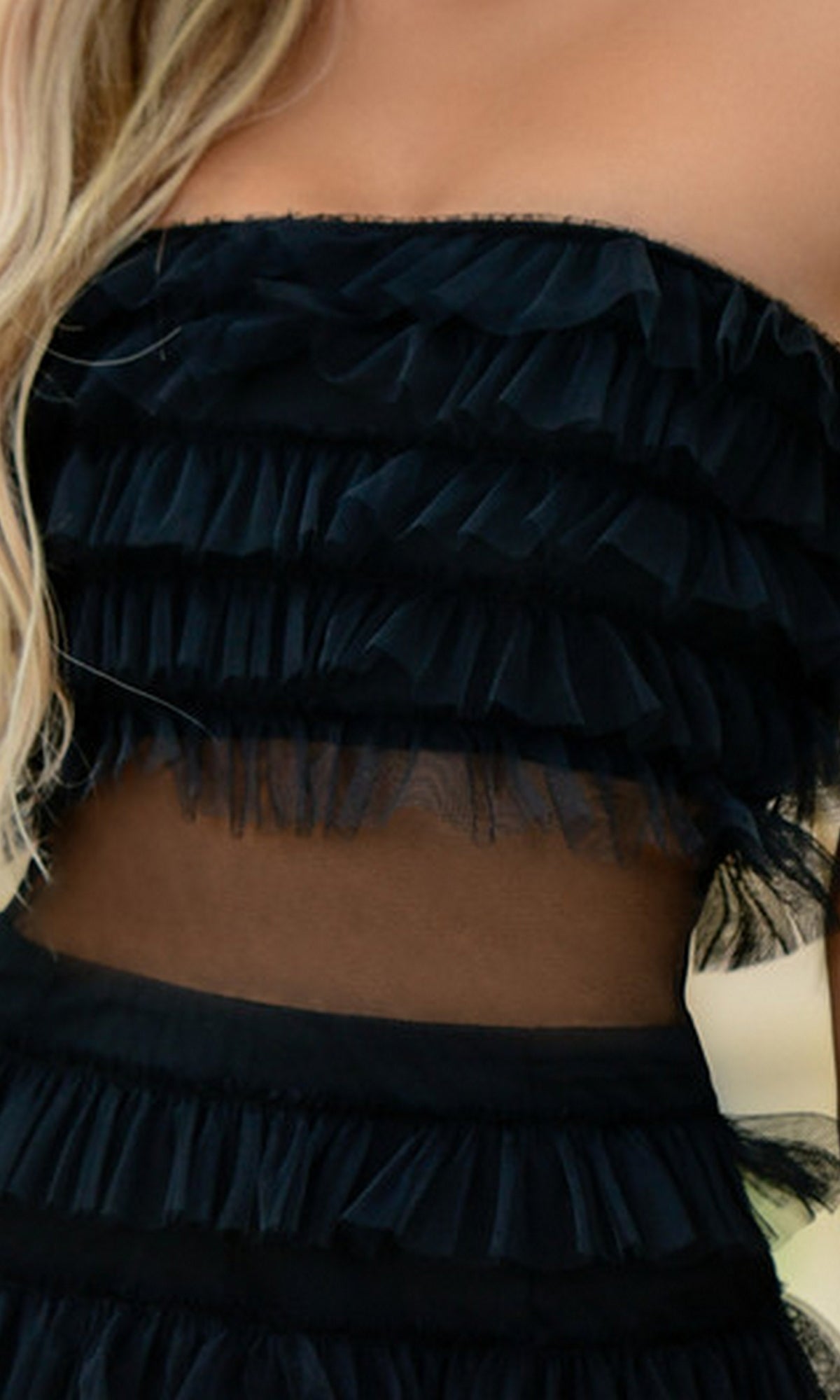 A close-up of a woman wearing the Velvi Georgia Tiered Short Strapless Hoco Dress, featuring layered ruffles and a sheer mesh midsection.